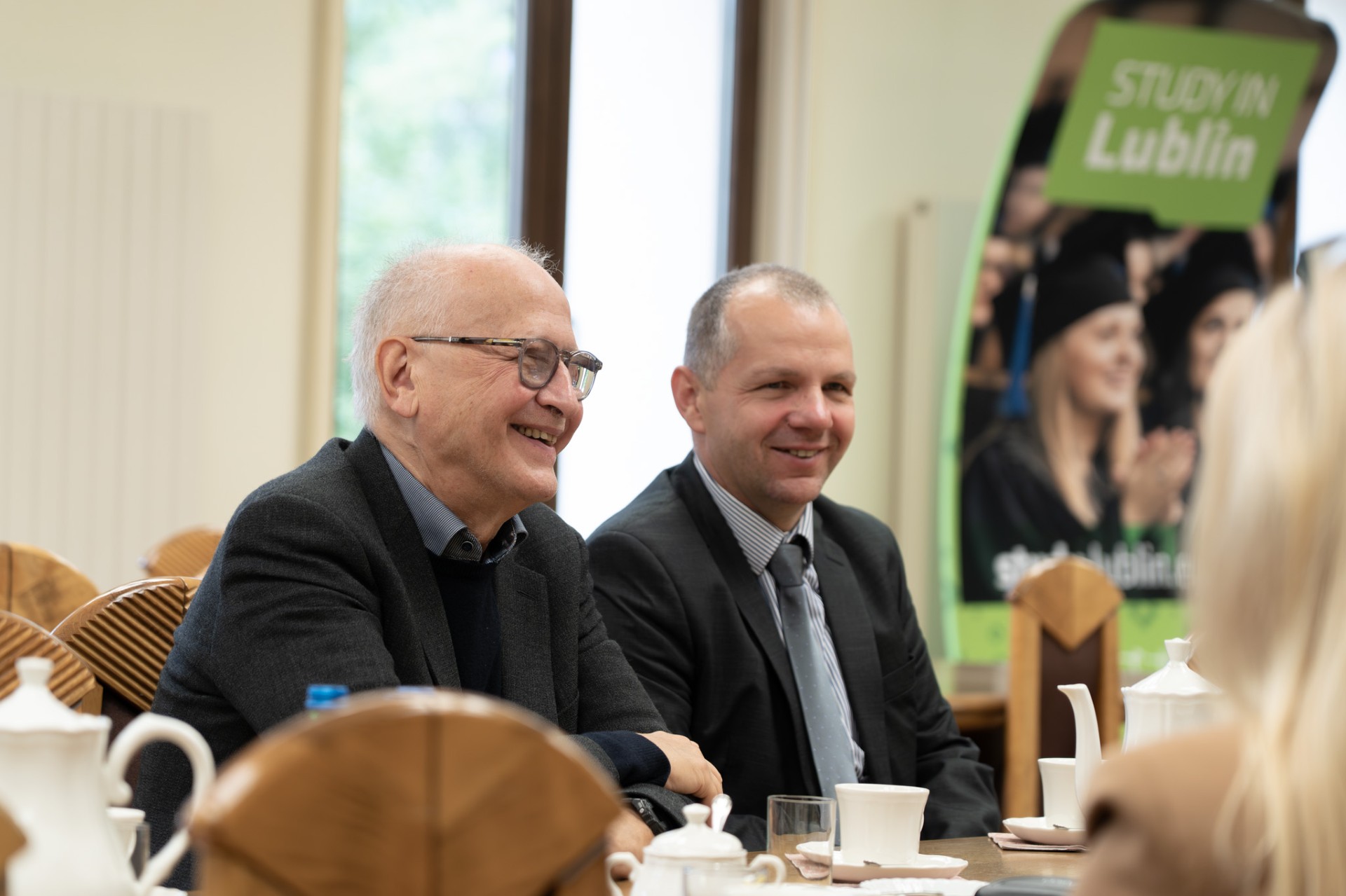 dwóch mężczyzn siedzi przy stole, śmieją się