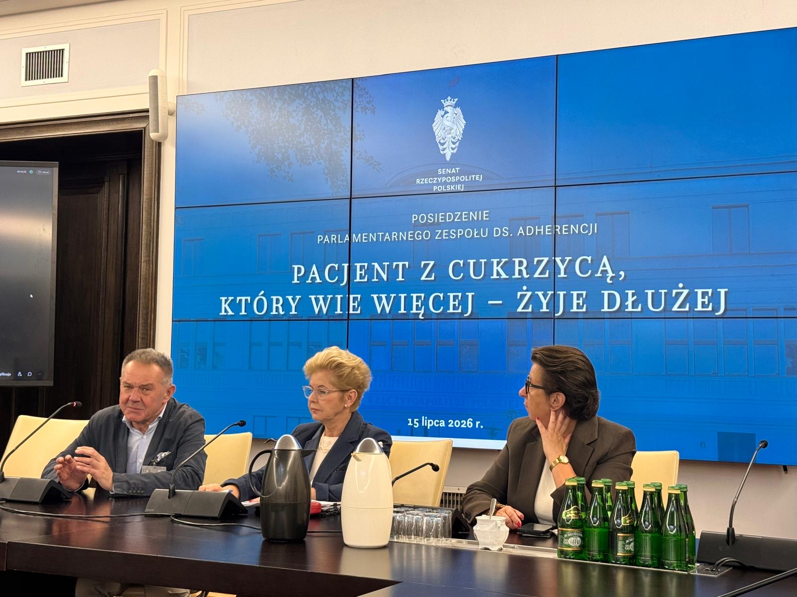 trzy osoby siedzą za stołem prezydialnym